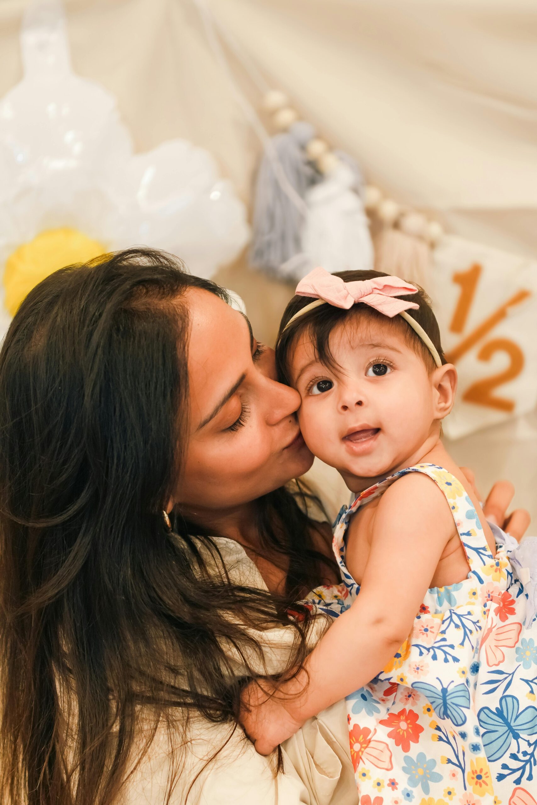 A loving mother kisses her baby's cheek during a charming half-birthday celebration.